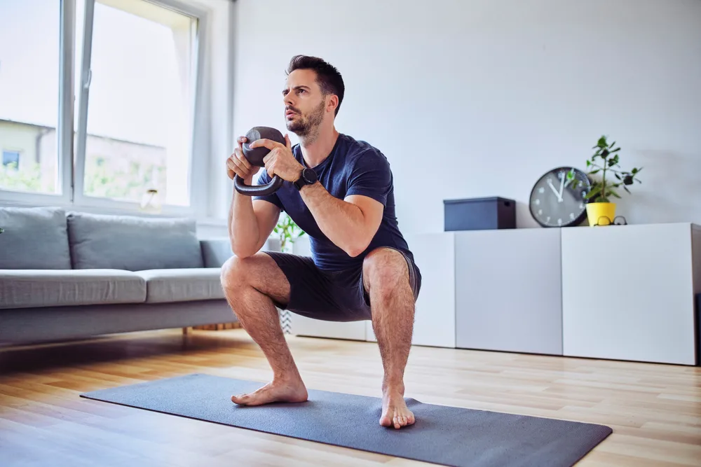 Training,At,Home,,Young,Man,Doing,Squats,With,Kettlebell,Weights.